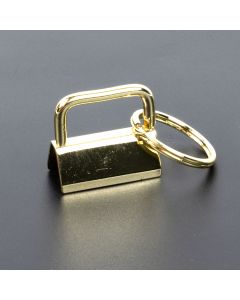 The image shows a gold-colored key fob hardware clamp (also called a key fob holder or webbing clamp) on a dark background
