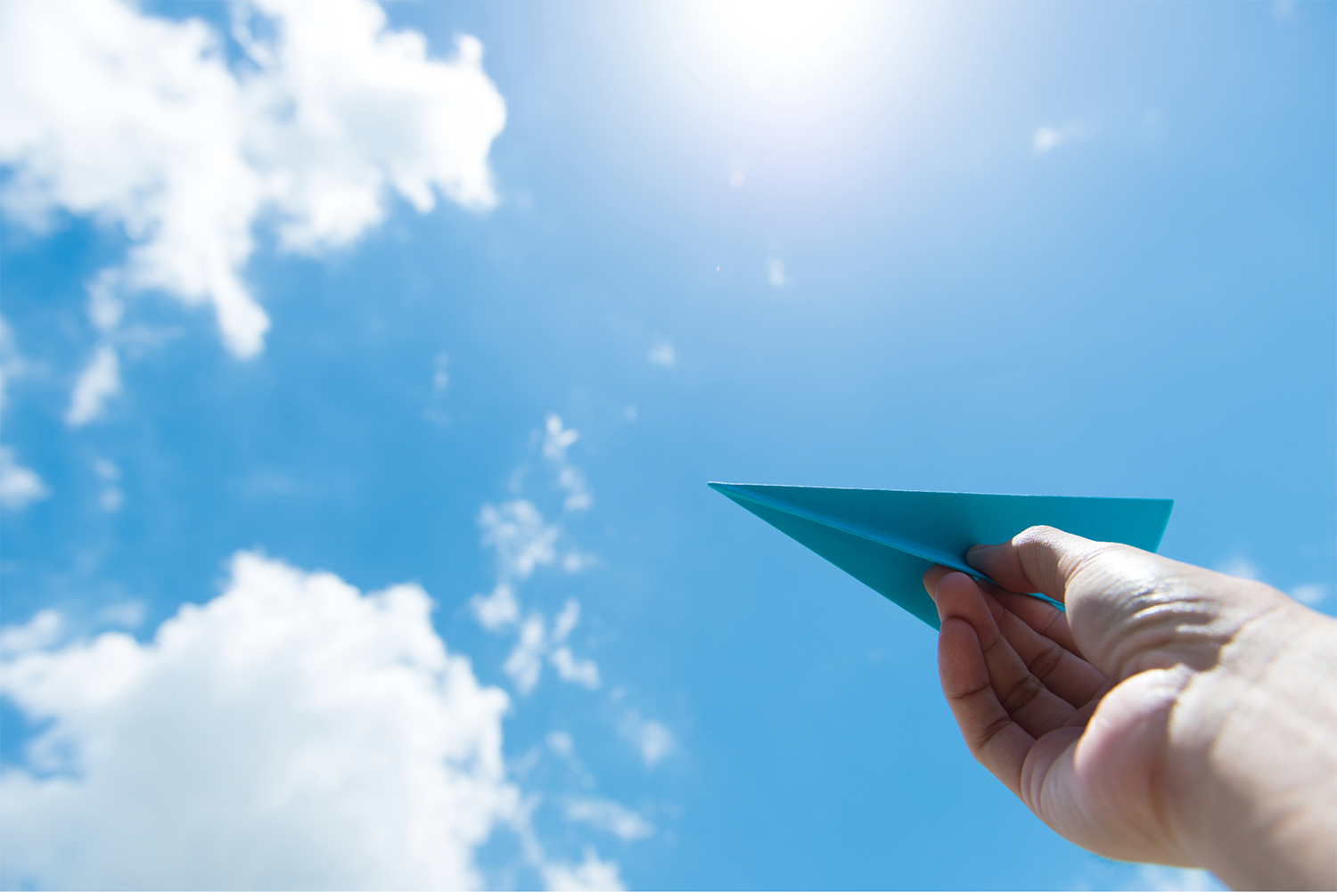 Blue paper airplane against a sunny blue sky