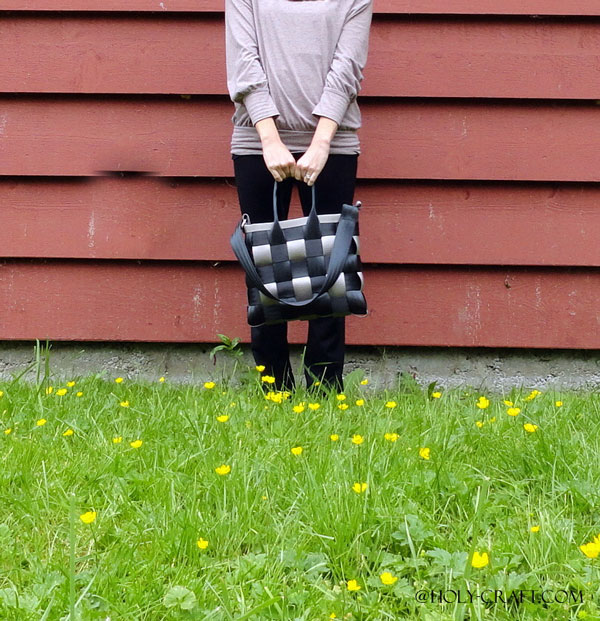 Woman standing against a barn with a black and gray woven handbag