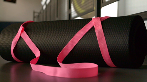 A black yoga mat with a pink strap